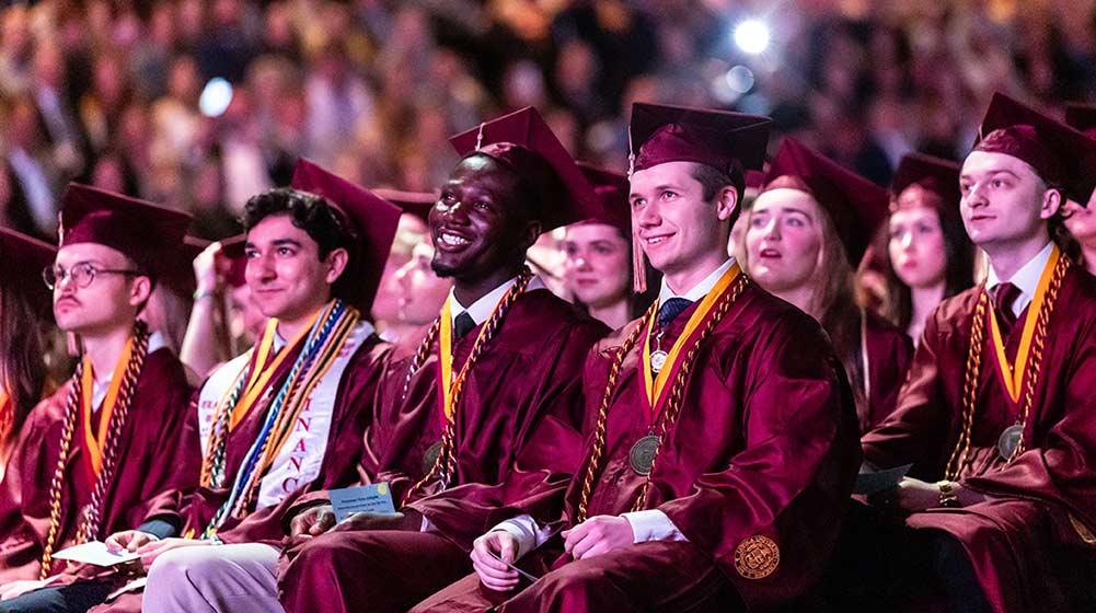 Students sitting at Commencement, dressed in their graduation gowns and mortarboards