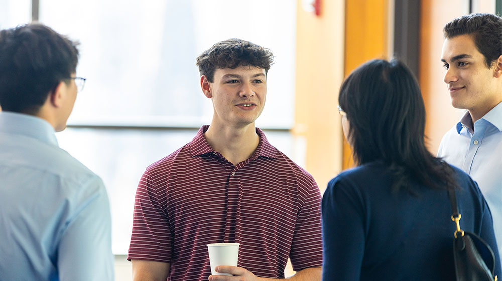 A student speaks with a group other students, alumni, and faculty
