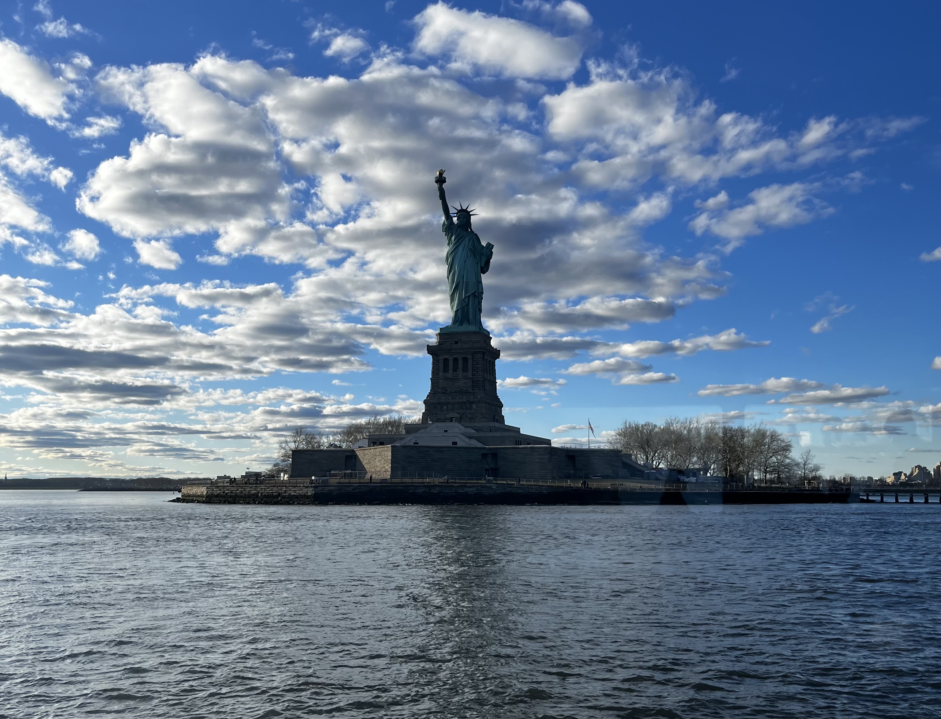 The Statue of Liberty stands tall among clouds and blue sky.