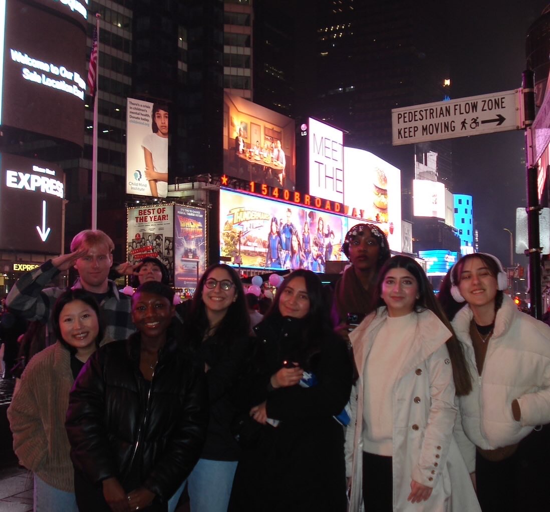 A group of students pose for a photo among the bright lights of NYC.