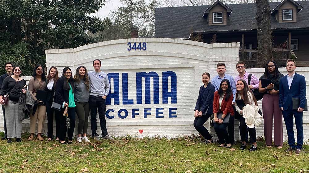 A group of students in front of a sign reading Alma Coffee