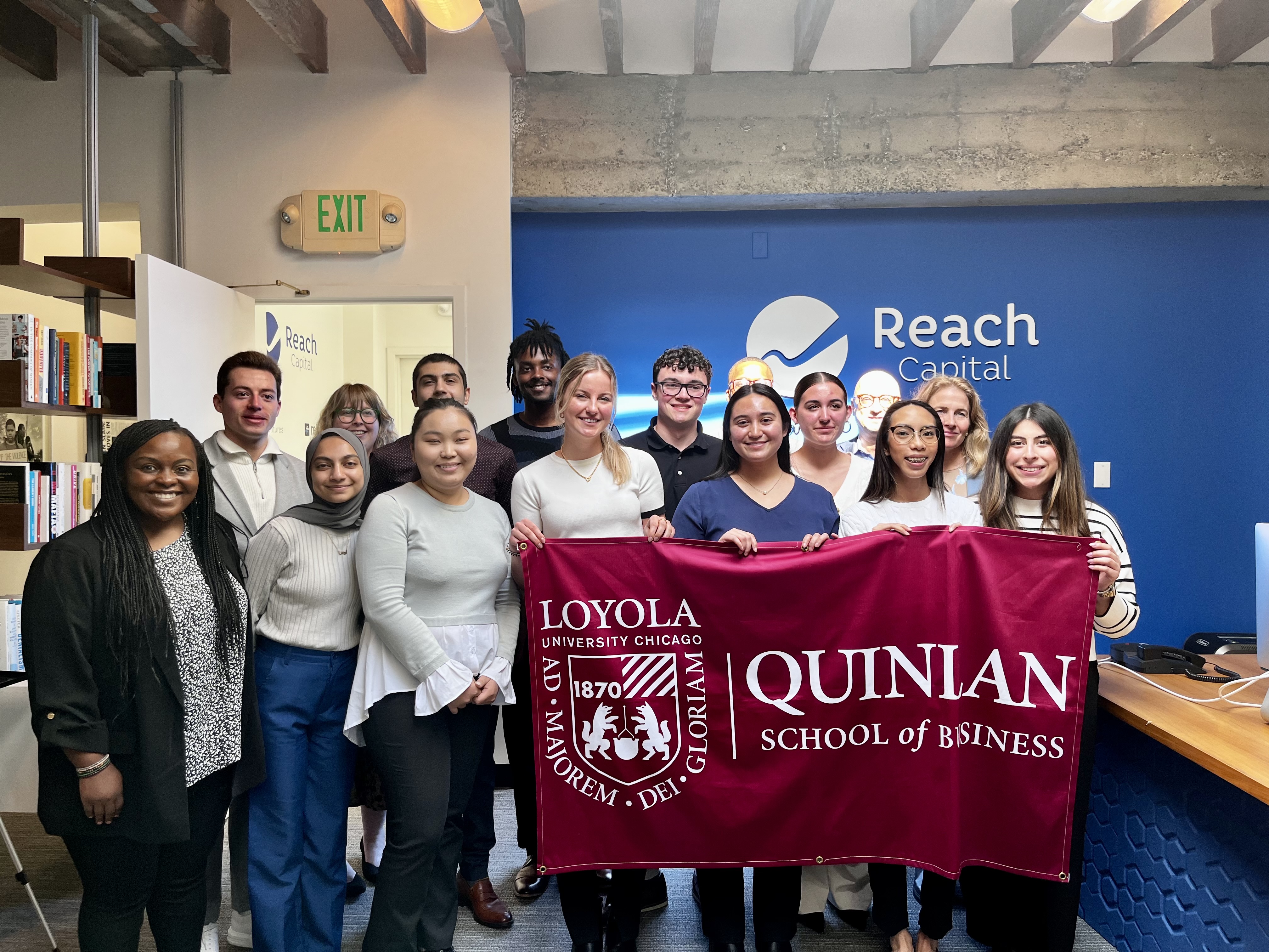 A group of students pose with the Quinlan flag inside the Reach Capital office in San Francisco.