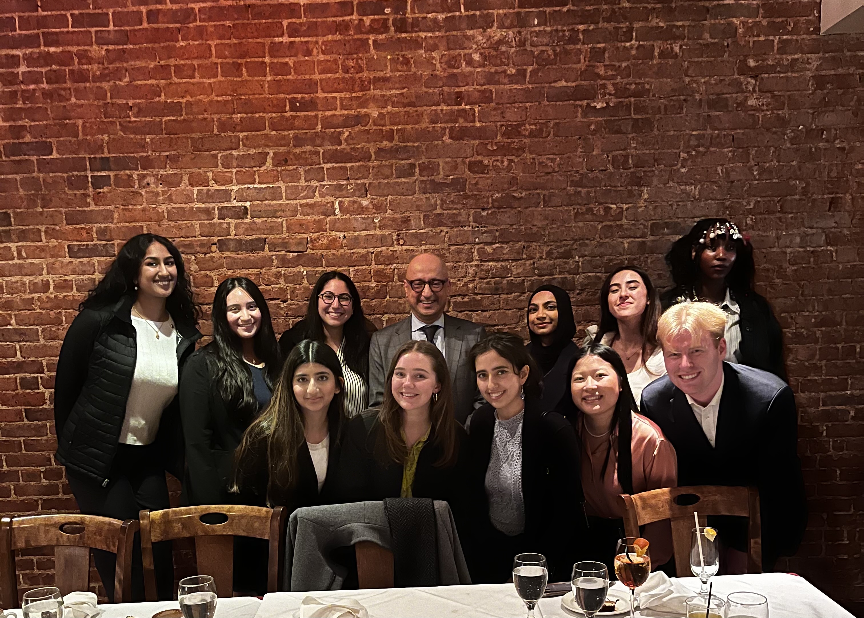A group of Ramble students pose for a photo with Dean Michael Behnam, with a red brick background.