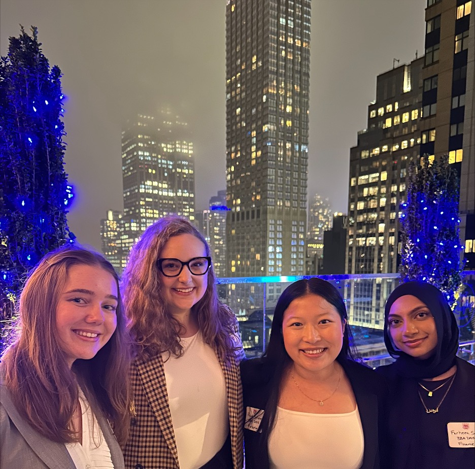 Three students and an alumna pose for a photo in front of the NYC skyline.