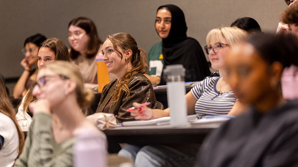 A group of students smile as they listen to the professor speak.