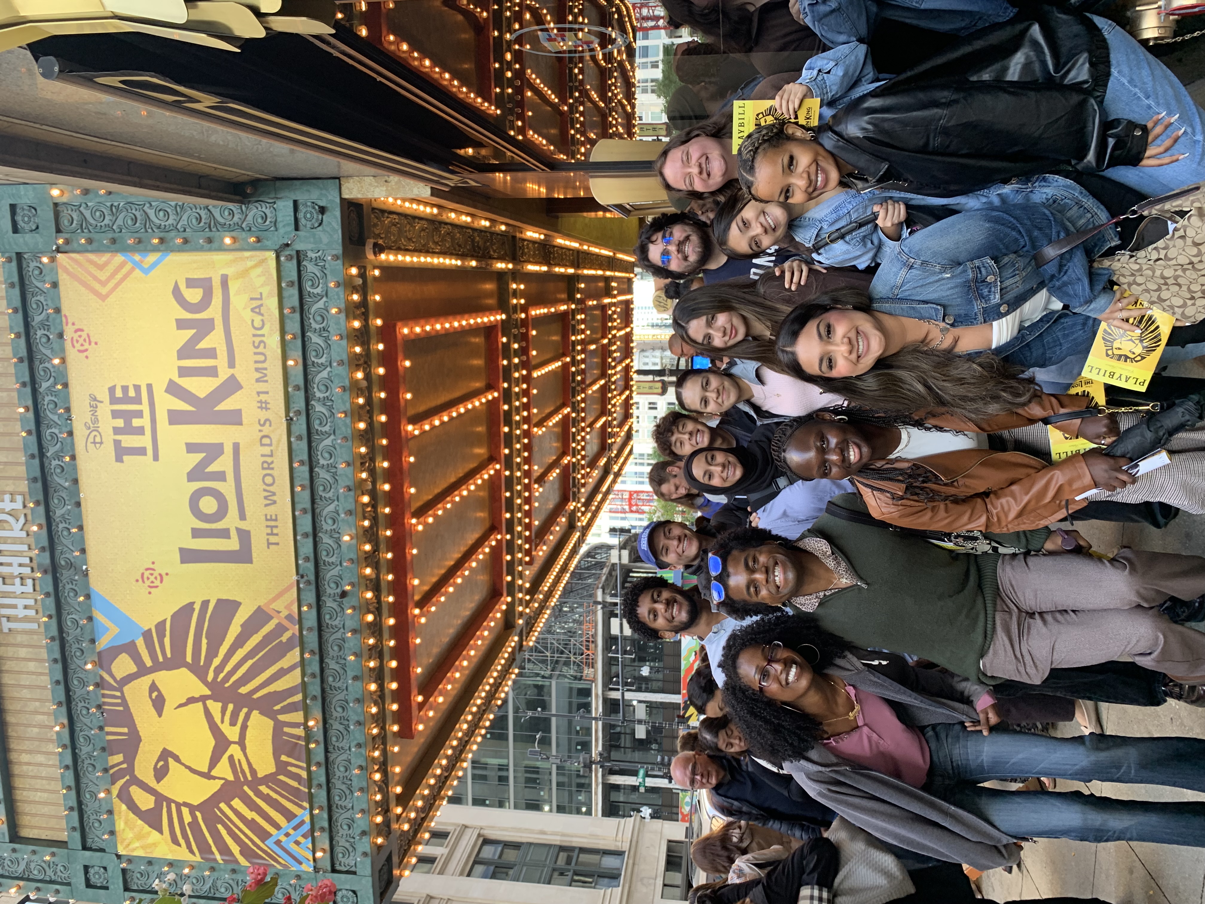 Loyola University Chicago's Leadership Scholars Program students gather near a sign after a performance of the Lion King on Broadway show in Chicago. The students are gathered together and smiling at the camera.