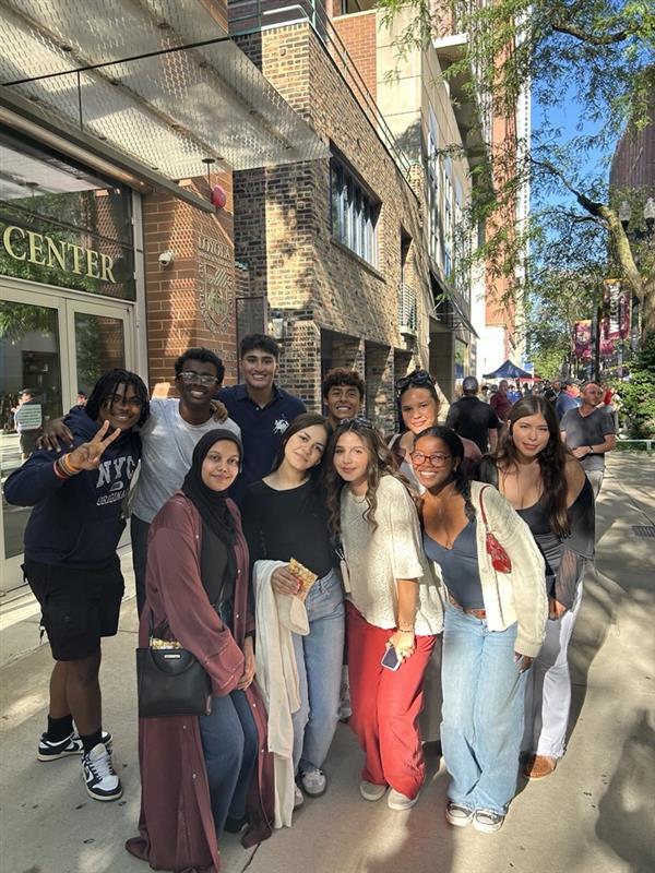 Loyola University Chicago Leadership Scholars Program Fall 2025 Cohort is outside the Schreiber Center at the Water Tower Campus. They are standing in two lines facing the camera and smiling.