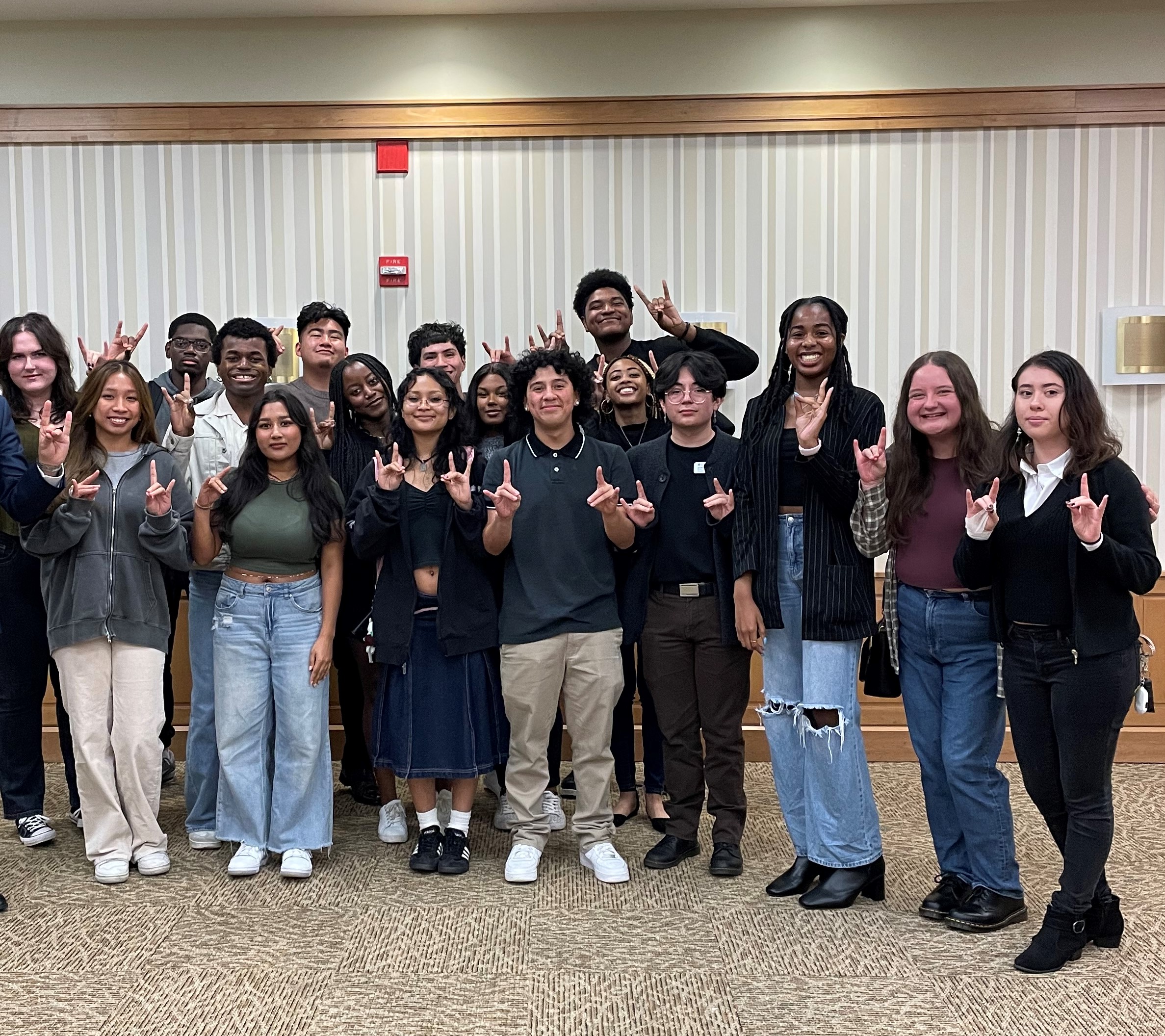 Loyola University Chicago Leadership Scholars Program Fall 2022 Cohort is in the Regis Residence Hall on the Lake Shore Campus. They are standing in two lines facing the camera, smiling, and sharing the LU Wolf hand symbol.