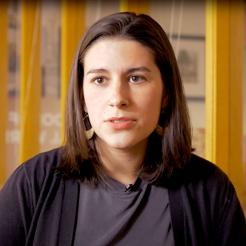 Sammi Shay sits indoors in front of a yellow-framed background.