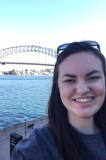 A selfie of Emily Tolley standing in front of a lake and bridge