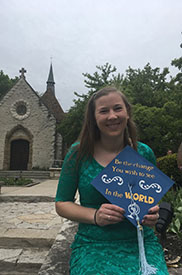Hannah Sternig holding a graduation cap standing in front of a church
