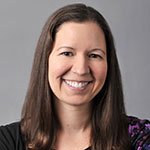 Jennifer Gamboa smiling, with straight shoulder-length brown hair, wearing a black top, against a neutral gray background.