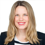 Rachael Persin, Internship Coordinator, with shoulder-length blonde hair and a bright smile, wearing a black blazer over a black-and-white striped top against a light background.