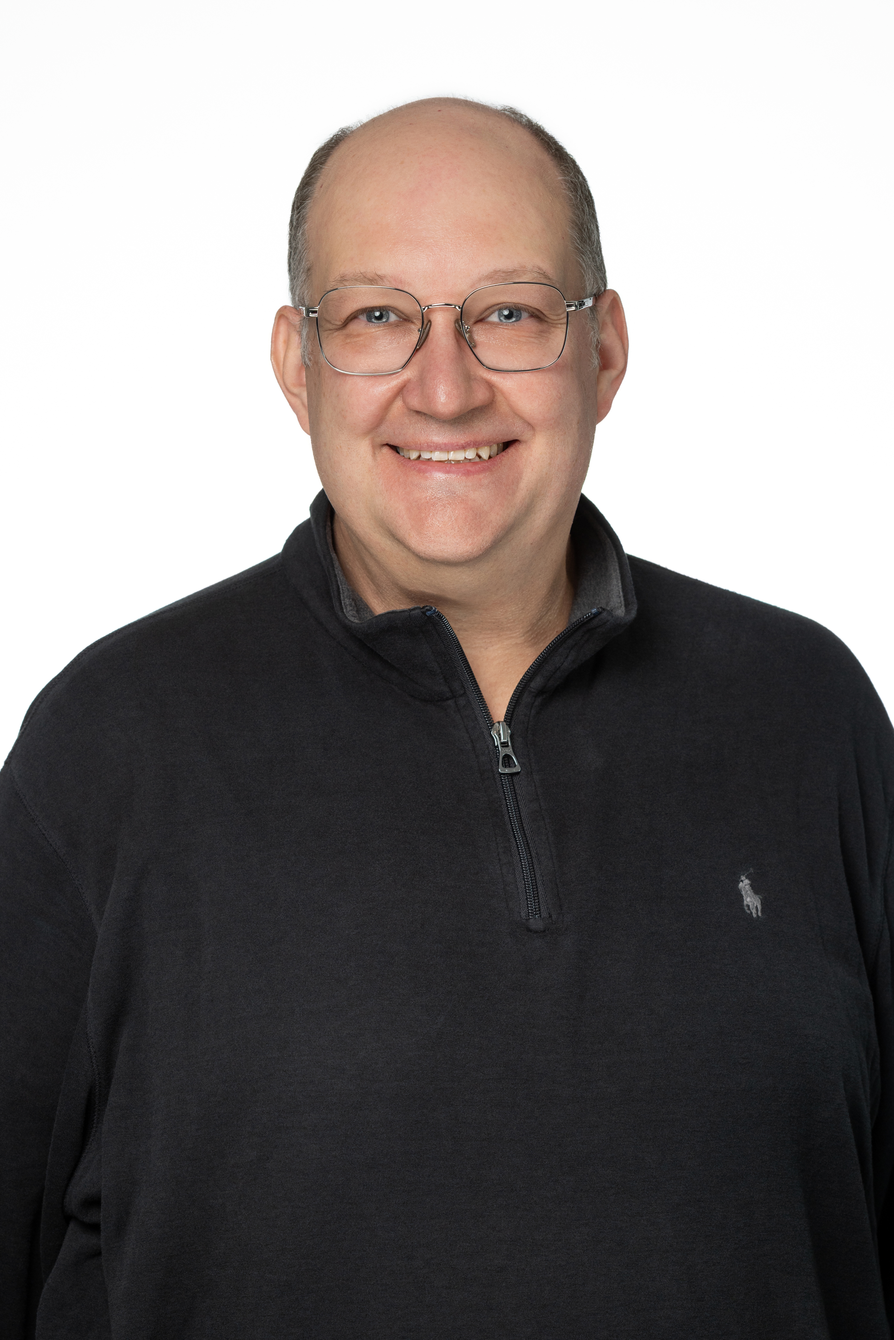 Nathan H. Perkins, a man with glasses and a bald head, wearing a dark quarter-zip pullover, smiling against a light gray background.