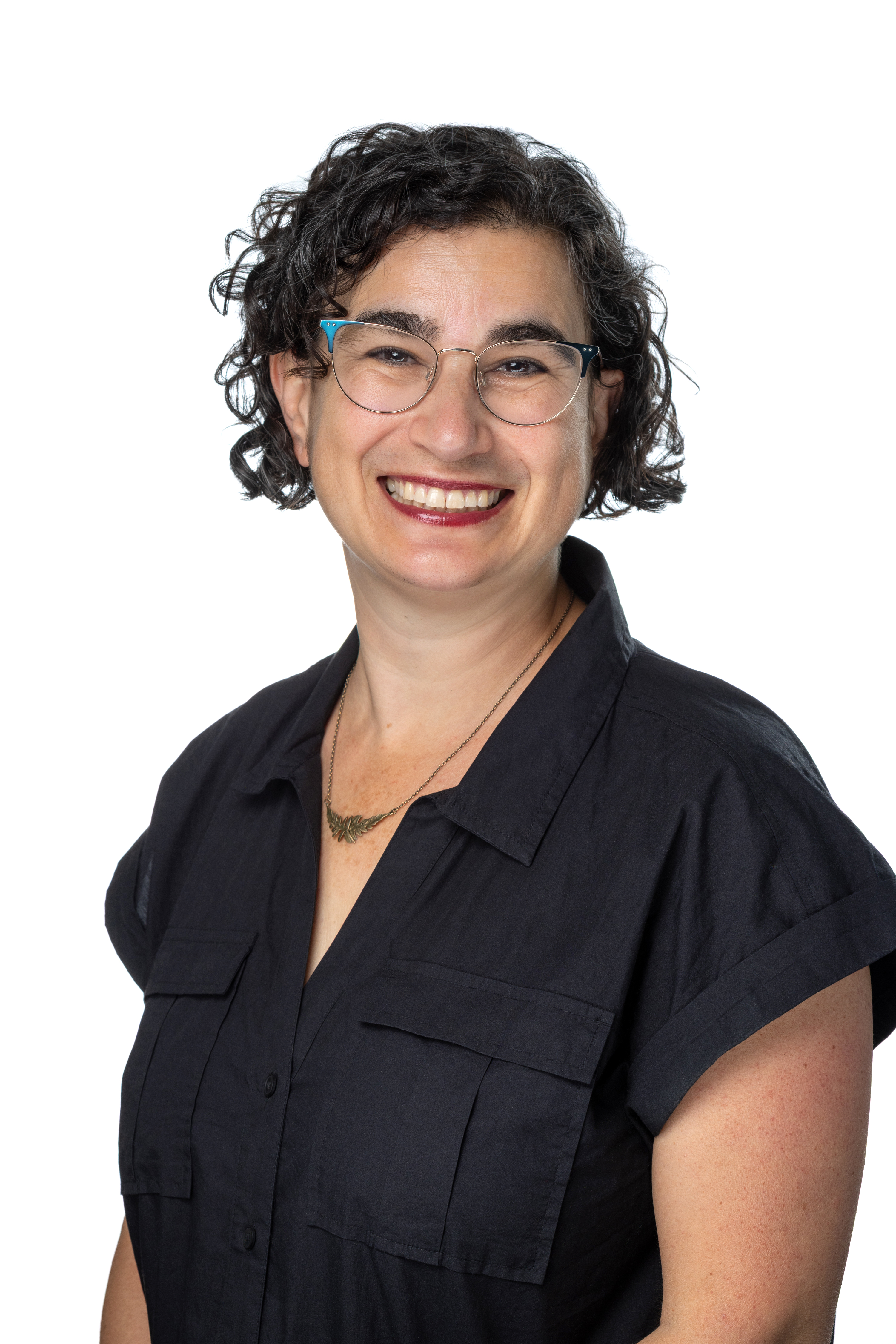 Sarah Lieberman Weisz, Director of Faculty Grants and Scholarship, smiling with short curly dark hair and glasses, wearing a navy short-sleeve blouse and a delicate necklace against a light background.