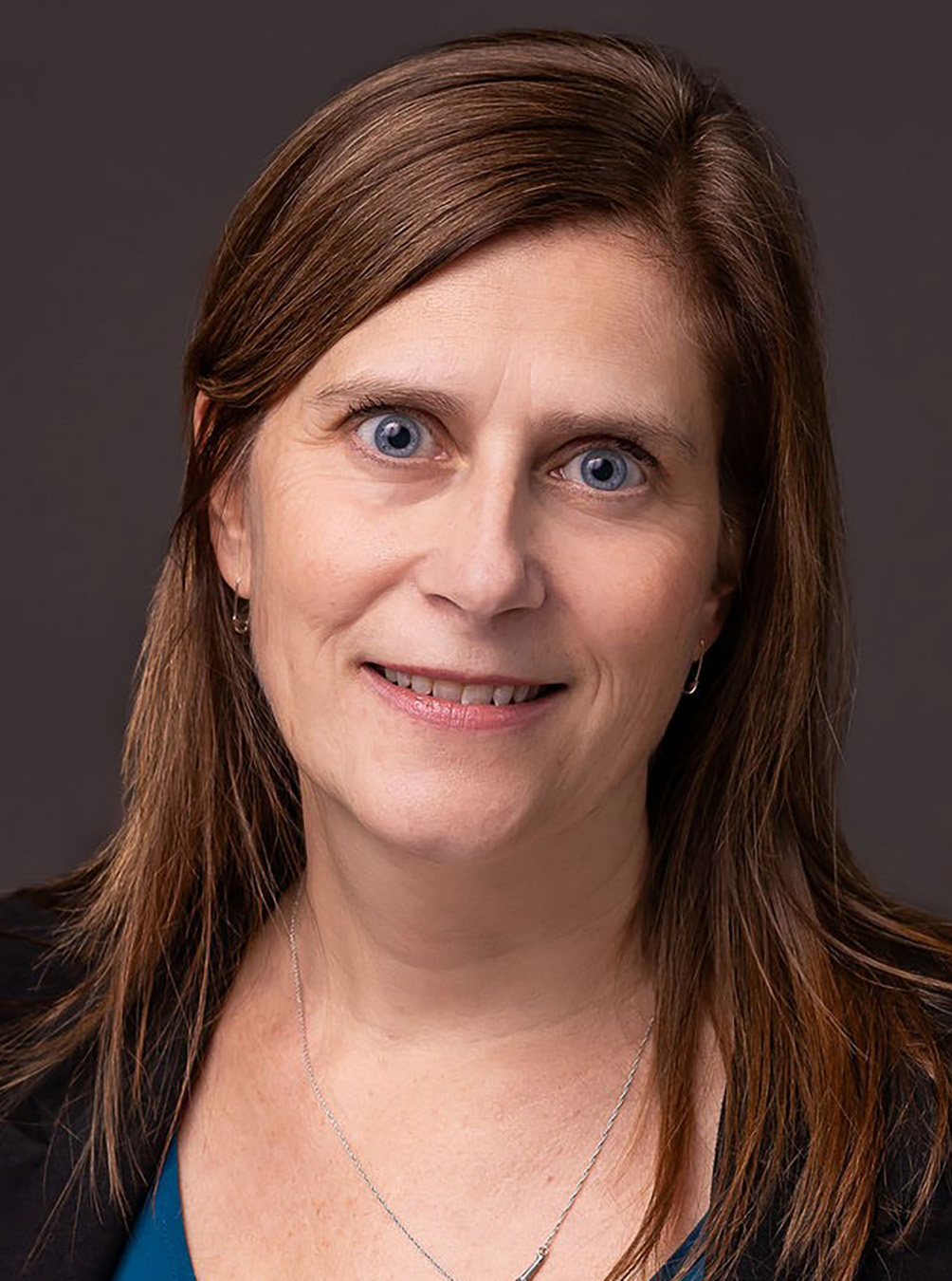 Woman with brown hair and blue eyes, wearing a dark blazer, against a neutral background.