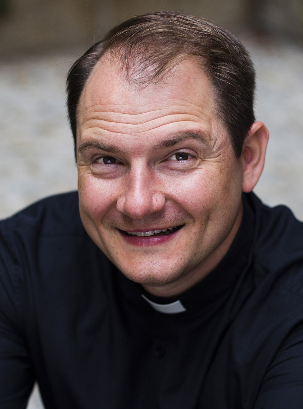 Man wearing a clerical collar, smiling at the camera.