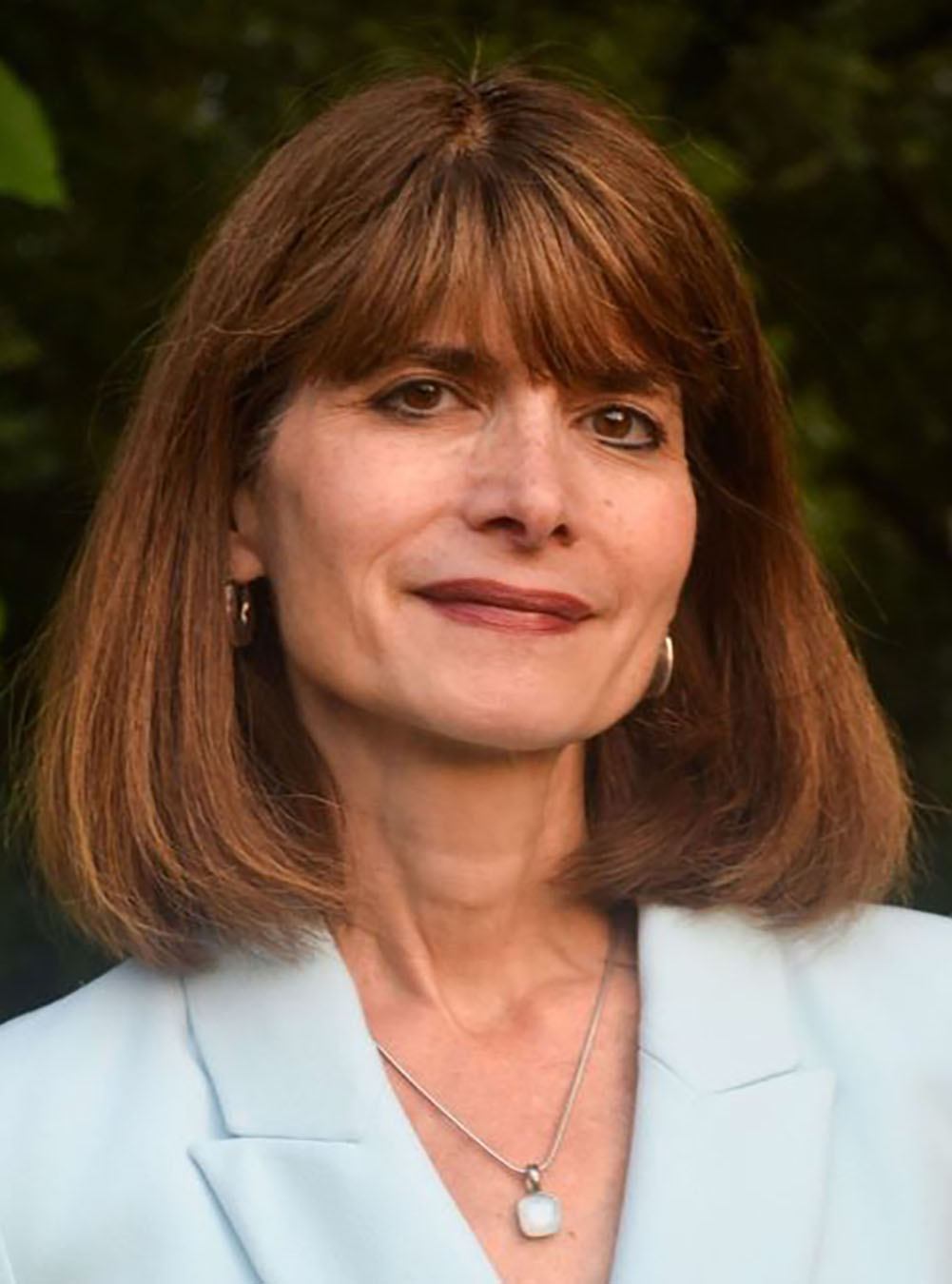 Woman with shoulder-length brown hair wearing a light blazer, photographed outdoors.