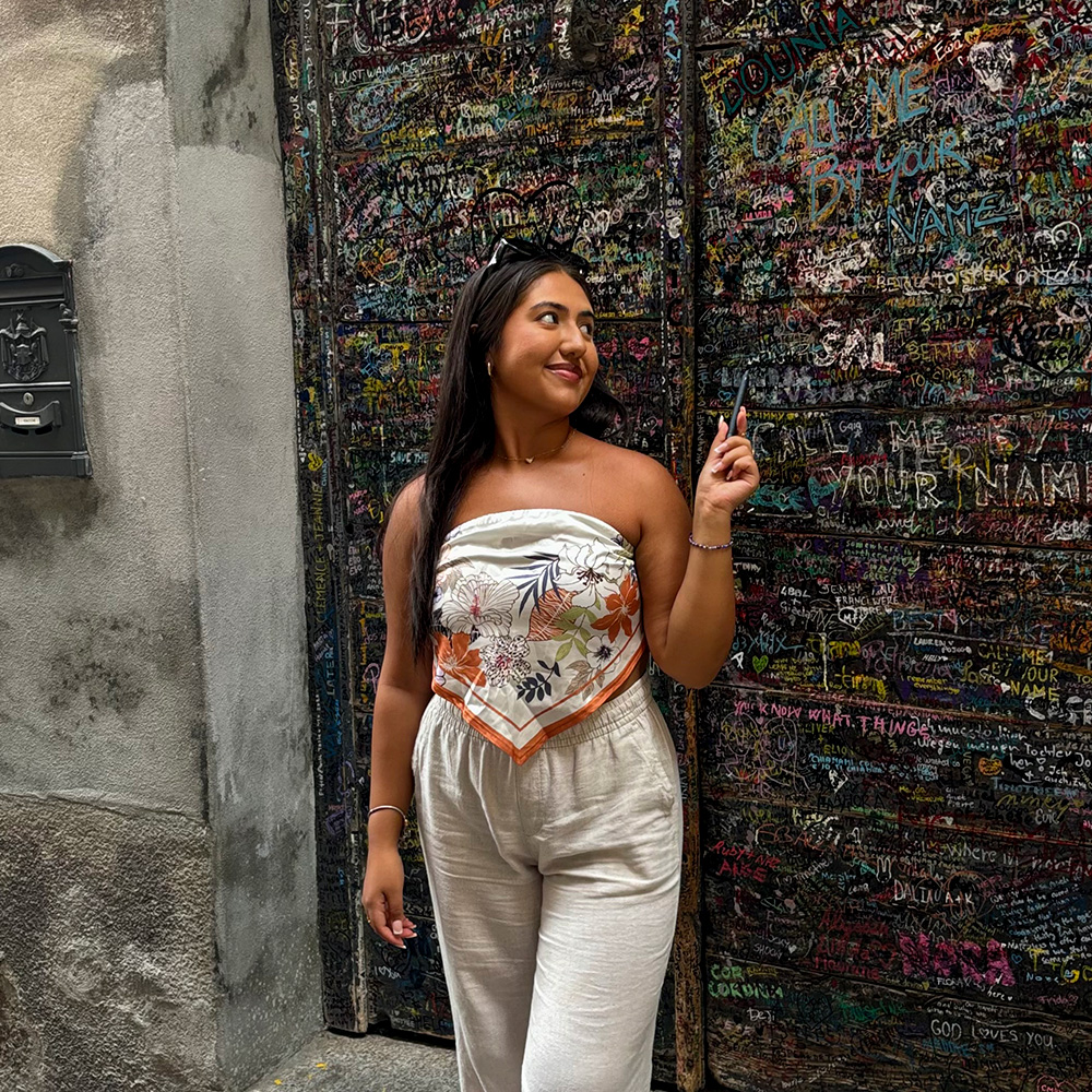 Melissa Ulloa stands in front of a board that displays hundreds of signatures and notes of travelers and others.