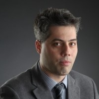 Man in a suit against a dark background, looking at the camera.