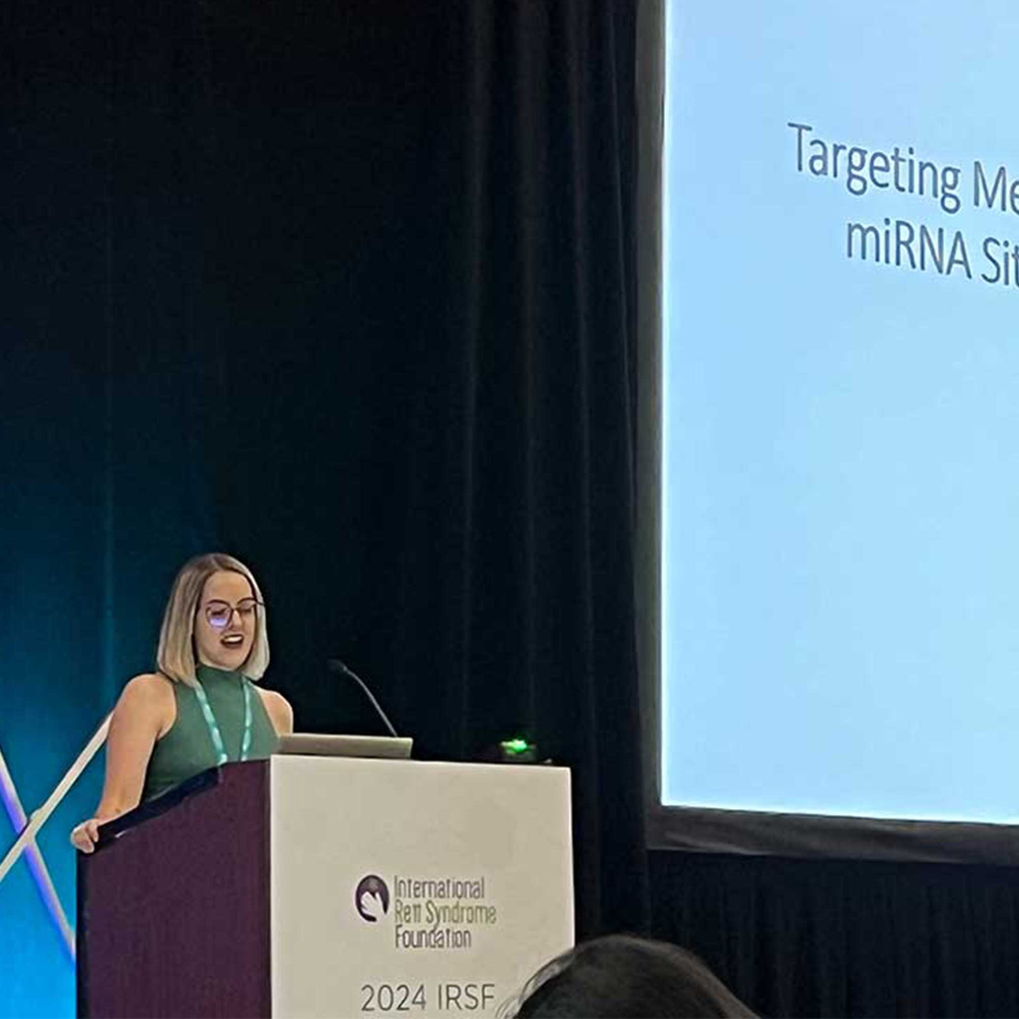 Amanda Vanderplow, PhD standing at a podium and speaking into a microphone