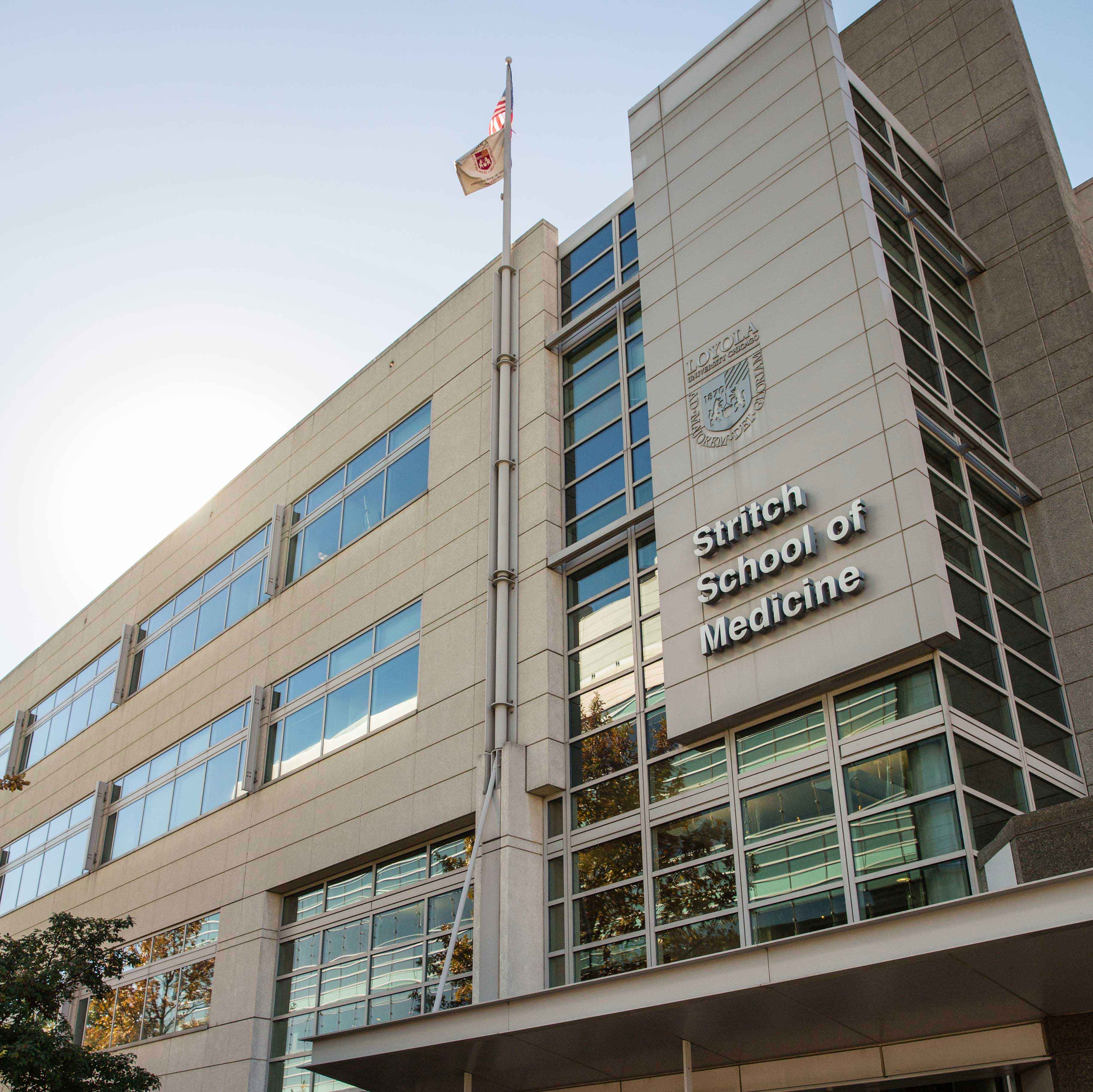 Stritch School of Medicine building with trees reflected in some windows and a light blue sky above